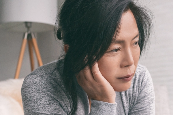 Adrenal-Fatigue-Doctor A middle-aged asian woman sitting on her couch, resting her head on her hand, suffering from adrenal fatigue. Get treatment for adrenal fatigue syndrome from Dr. Noelani Rodriguez in San Diego.