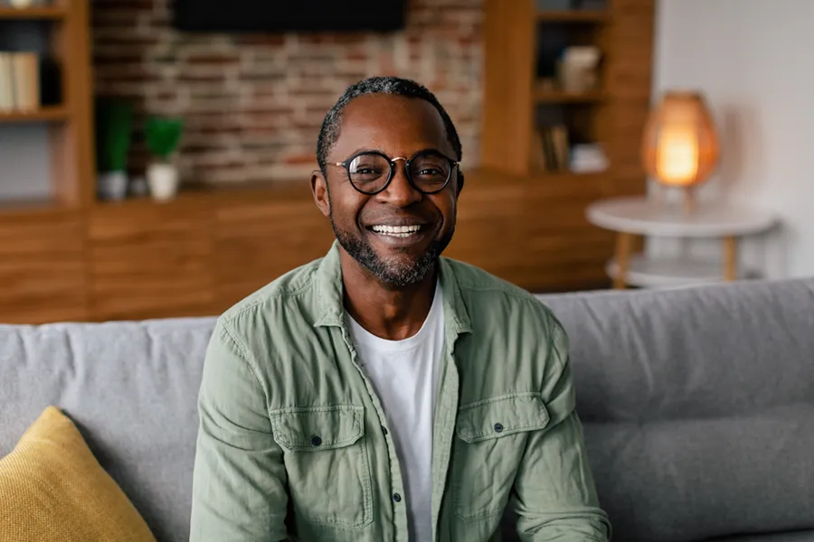 Andropause-Doctor A middle aged black man in a green button up shirt sits on his couch smiling, happy with his treatment for andropause and low testosterone from Dr. Noelani Rodriguez in San Diego.