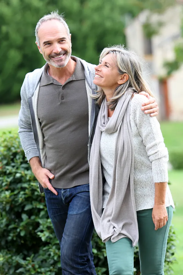 Bioidentical-Hormone-Therapy-Treatment A mature couple in gray toned clothes and jeans walk happily outside, happy with their successful bioidentical hormone treatments from Dr. Noelani Rodriguez in San Diego.