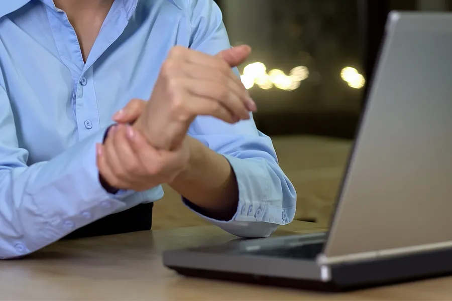 Carpal-Tunnel-Syndrome-Clinic A woman sits in front of her computer rubbing her hand in pain. Schedule treatment for carpal tunnel syndrome from Dr. Noelani Rodriguez in San Diego.