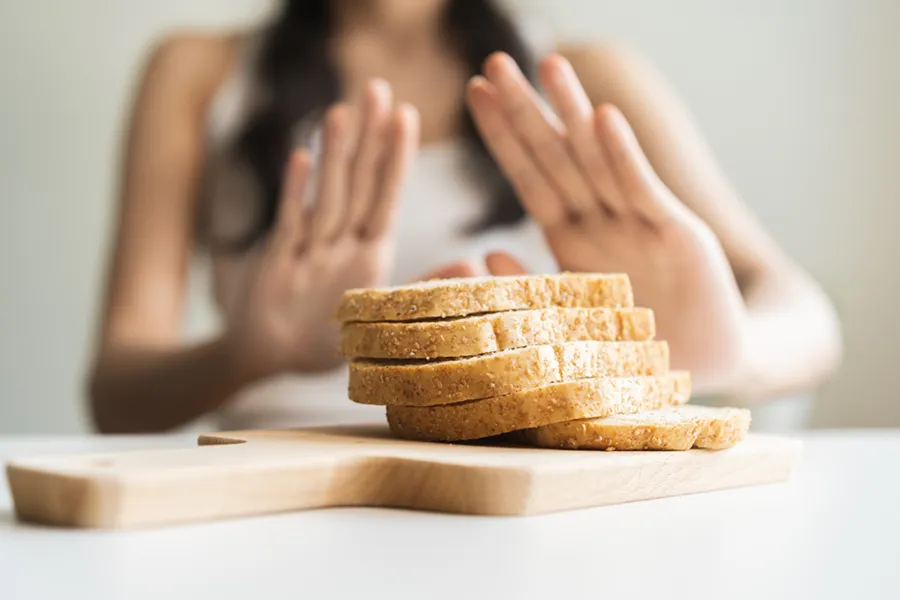 Celiac-Disease-Clinic Close up of a stack of bread slices on a cutting board with a woman's hands behind them, refusing to eat. Get treatment for Celiac Disease from Dr. Noelani Rodriguez in San Diego.