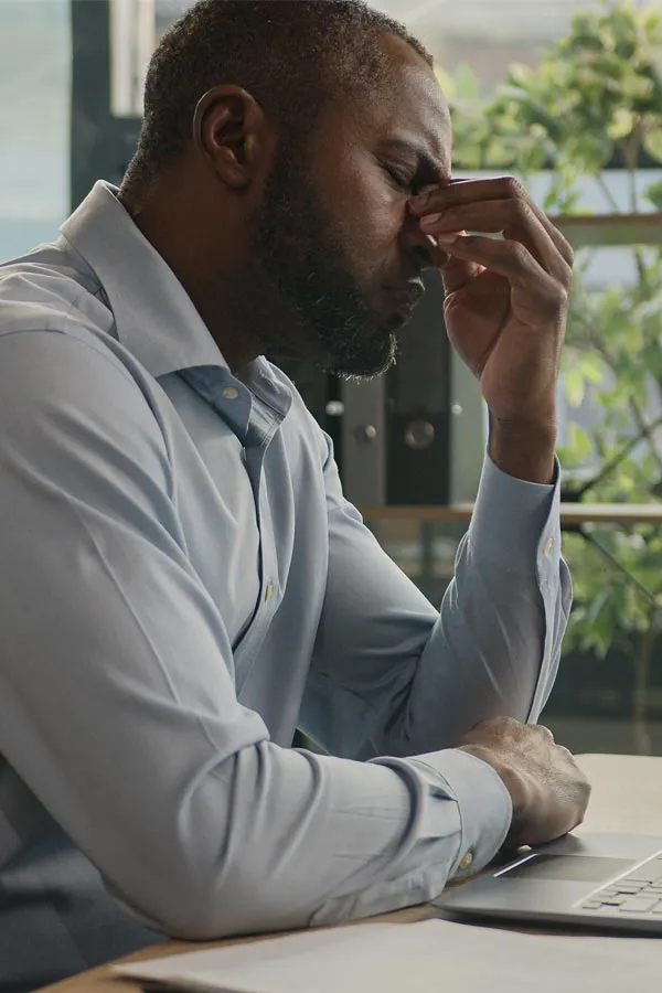 Chronic-Fatigue-Treatment A black man rubbing the top of his nose at his desk, in need of chronic fatigue treatment from Dr. Noelani Rodriguez in San Diego.