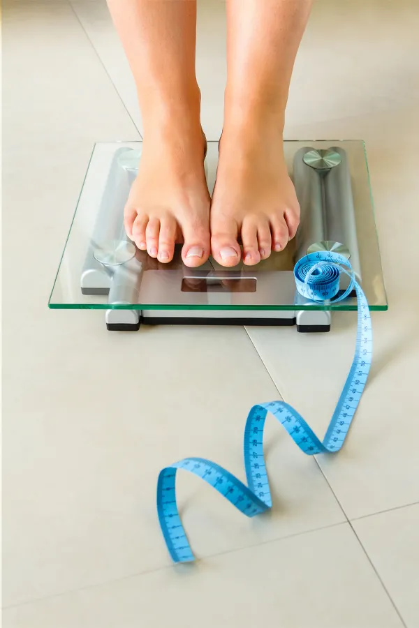 HCG-Weight-Loss-Resistance-Treatment A close-up of feet on a digital glass scale with a blue measuring tape. Dr. Noelani Rodriguez in San Diego provides HCG weight loss injections designed to break through stubborn metabolic plateaus.