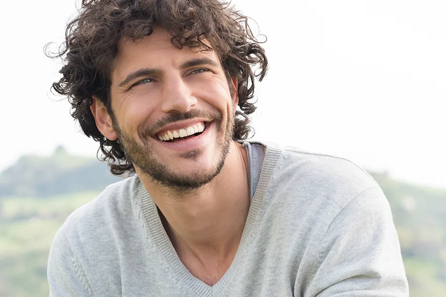 Hair-Loss-Clinic A man with radiant curly hair and a confident smile looks to the horizon. Dr. Noelani Rodriguez in San Diego offers effective therapies to support hair regrowth and scalp health to treat hair loss.