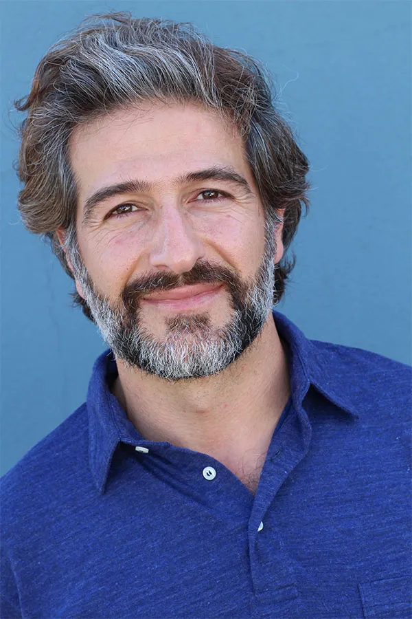 Hair-Loss-Treatment Image of a cheerful man with a bright smile and curly hair against a natural landscape. Dr. Noelani Rodriguez provides personalized hair loss treatments in San Diego.