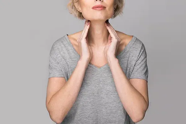Hashimotos-Thyroiditis-Doctor An older blonde woman in a gray t-shirt holds her hands to her neck checking for signs of thyroid problems. Get help for Hashimoto's Thyroiditis from Dr. Noelani Rodriguez in San Diego.