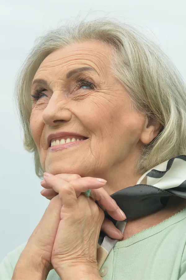 Hot-Flashes-and-Night-Sweats-Treatments An older woman holds her hands together under her chin and looks up at a cool sky smiling. Get treatment for hot flashes and night sweats from Dr. Noelani Rodriguez in San Diego.