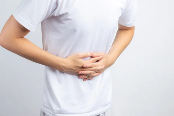 Irritable-Bowel-Syndrome-Clinic A person holding their stomach in visible discomfort against a plain background. Dr. Noelani Rodriguez treats irritable bowel syndrome with functional medicine in San Diego.