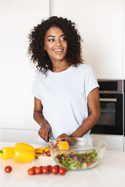 Irritable-Bowel-Syndrome-Treatment Image featuring a smiling woman chopping vegetables for a salad in a bright, white kitchen. Dr. Noelani Rodriguez offers Irritable Bowel Syndrome Treatment and Digestive Support in San Diego.