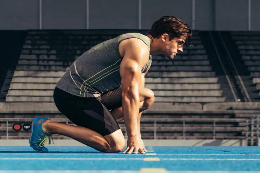 Lean-Muscle-and-Recovery-Clinic A white man kneels at the starting line on a track, determined to do his best. Get treatment for lean muscle loss and recovery from Dr. Noelani Rodriguez in San Diego.