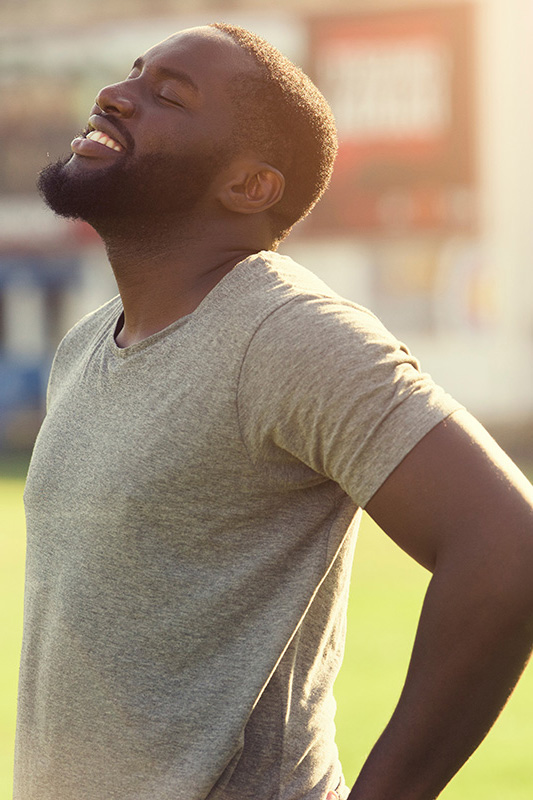 Lean-Muscle-and-Recovery-Treatment A black man in a gray t-shirt and smiles, looking up with closed eyes after a satisfying workout. Get treatment for lean muscle loss and recovery from Dr. Noelani Rodriguez in San Diego.