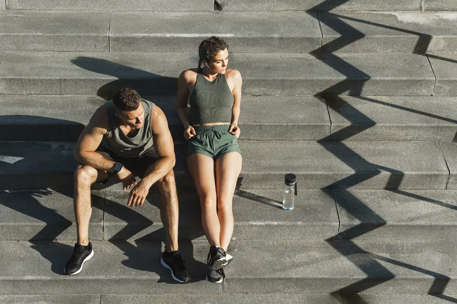 Medical-Weight-Loss-Doctor A couple in gray and green track clothes resting after a workout on stone steps, happy with their weight loss plans from Dr. Noelani Rodriguez in San Diego.