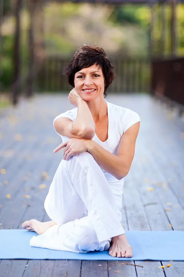 Osteoporosis-Treatment A middle-aged woman happily sits in a yoga pose. Get Osteoporosis treatment from Dr. Noelani Rodriguez in San Diego.