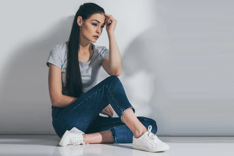 PCOS-Doctor A young brunette woman in a gray t-shirt and jeans sits against a gray wall with her head resting on her hand and a distressed expression. Get help for Polycystic Ovarian Syndrome (PCOS) from Dr. Noelani Rodriguez in San Diego.