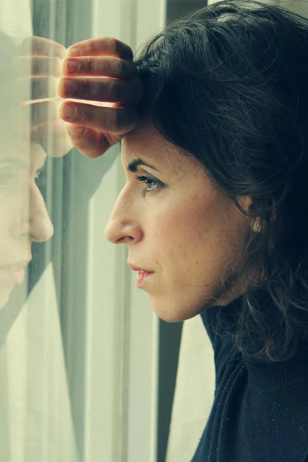 PCOS-Treatment A brunette woman in a thin dark turtleneck looks out the window with a serious expression, suffering from PCOS. Get treatment for Polycistic Ovarian Syndrome/PCOS from Dr. Noelani Rodriguez in San Diego.