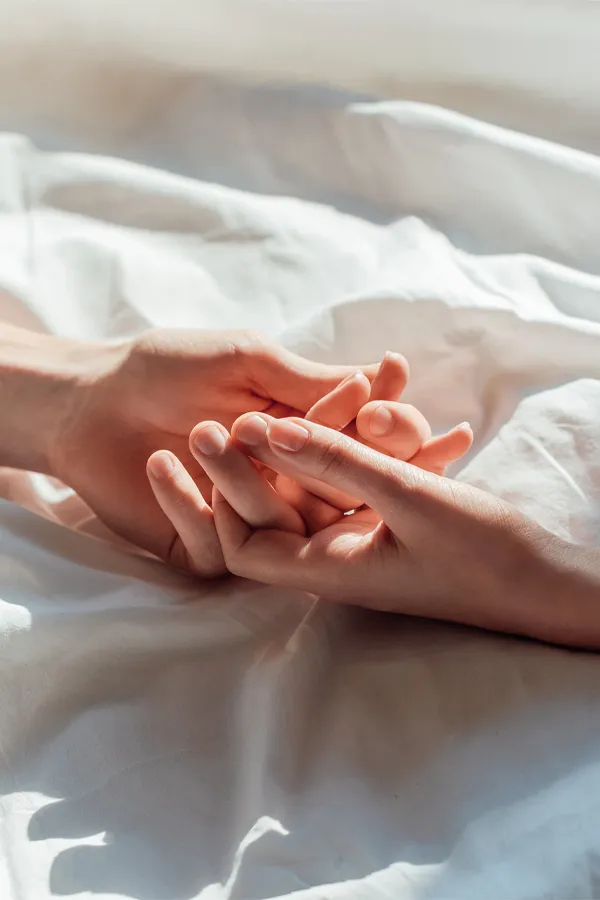 PT141-for-Women-Treatment A close up of a man and woman's hands lightly clasping on a bedsheet, representing successful PT141 sexual wellness treatment for women from Dr. Noelani Rodriguez in San Diego.