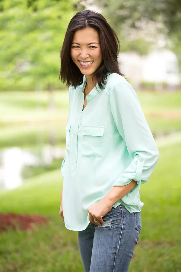 Perimenopause-Treatment A middle-aged brunette woman in a light green button-up shirt stands outside smiling, happy with her perimenopause treatment from Dr. Noelani Rodriguez in San Diego.