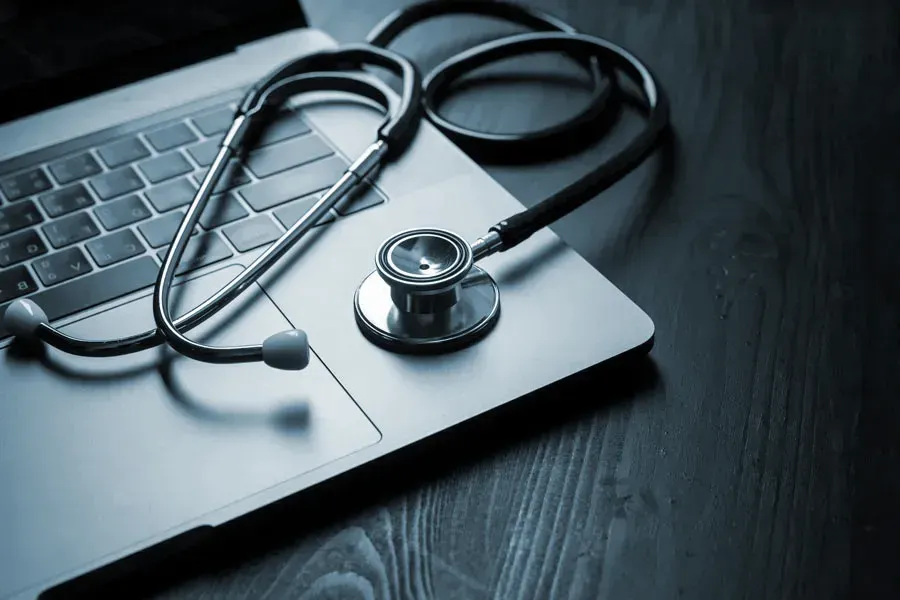 Telemedicine-Doctor An open laptop with a stethoscope lying on it on a wooden table, symbolizing telemedicine care from Dr. Noelani Rodriguez in San Diego.