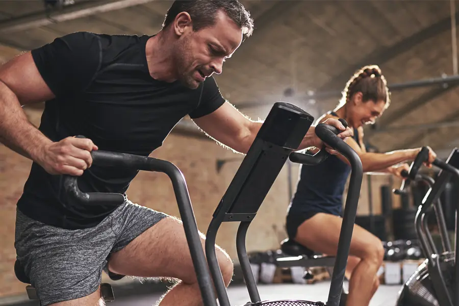 Tirzepatide-Doctor A couple in a brick gym work as hard as they can on exercise bikes, inspired by successful Tirzepatide treatment from Dr. Noelani Rodriguez in San Diego.