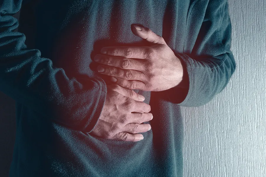 Ulcerative-Colitis-Clinic Close-up of the midsection of a man in a green sweater clutching his gut in pain. Get treatment for Ulcerative Colitis from Dr. Noelani Rodriguez in San Diego.