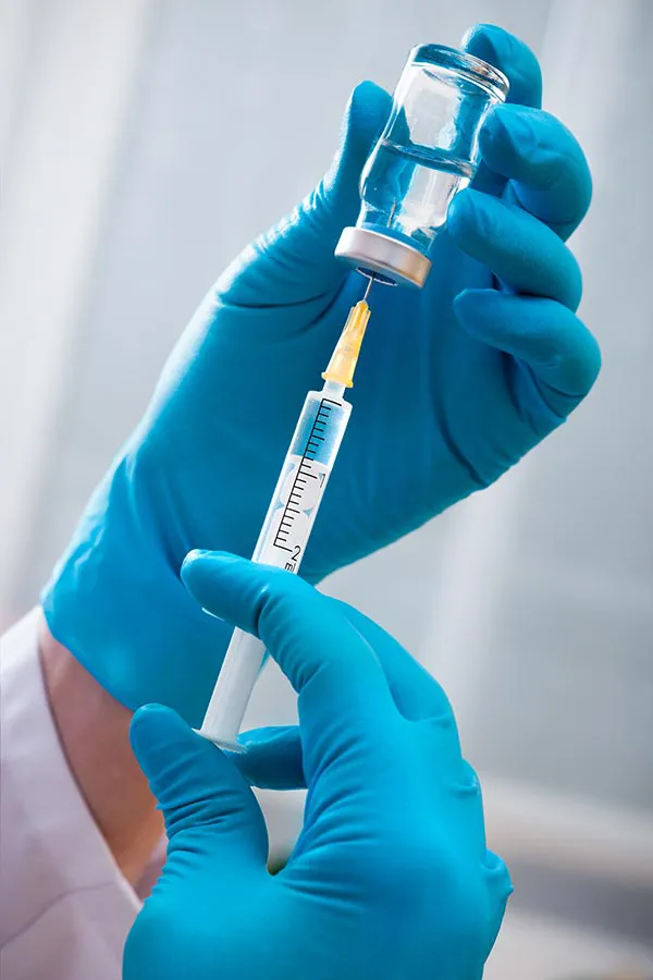 Vitamin-Injection-Treatment Close-up of hands in blue medical gloves drawing fluid from a vial into a syringe, representing vitamin injections from Dr. Noelani Rodriguez in San Diego.